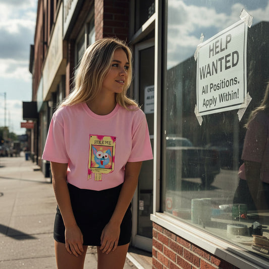 Woman wearing a pink t-shirt with a graphic design standing in front of a store window with a 'Help Wanted' sign.